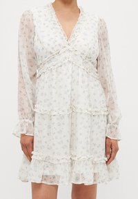 Witte bloemenjurk met ruches, gelaagd ontwerp, lange transparante mouwen en een V-hals. Lichtblauwe en groene bloemenpatronen.