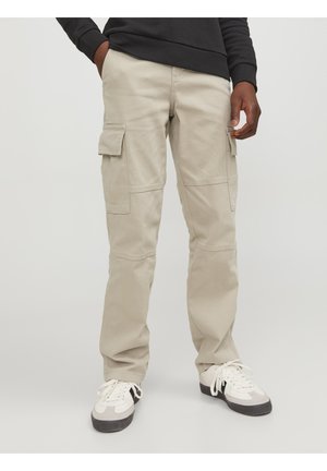 Pantalones cargo beige de algodón, con bolsillos laterales, corte relajado y detalles de costuras visibles. Combinados con zapatillas blancas.