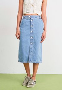 Jeans-Midirock in Hellblau mit geradem Schnitt, versehen mit einer Reihe von metallischen Druckknöpfen auf der Vorderseite und einem leicht fransigen Saum.