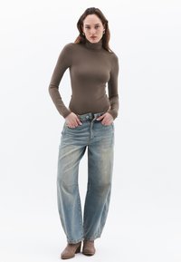 Bruine lange mouw turtlenecktop gecombineerd met lichtgewassen, loszittende denim jeans met een knoopsluiting en voorzakken. Bruine haklaarzen.