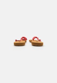 Red flip-flops featuring a knotted fabric strap, brown textured sole, and flat design. The straps display a polka dot pattern.