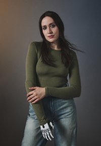 Langermet oliven grønn topp kombinert med høyt liv blå denimjeans; har en hvit protetisk hånd med svarte aksenter.