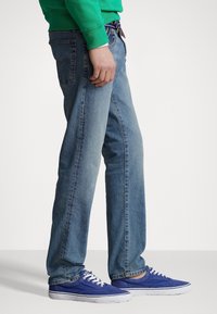 Světlé modré džíny s rovnou siluetou, obsahující pět kapes a kontrastní šití. Kombinované s modrými teniskami.