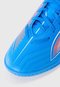 Bout de chaussure de sport bleu avec des accents orange et blanc, surface texturée et lacets bleus sur un fond blanc.