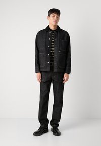 Jachetă din denim negru cu buzunare cu clapetă, închidere cu nasturi, asociată cu pantaloni din denim negru asortați. Cămășă cu dungi negre și verzi dedesubt.