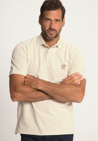 Polo beige con colletto, maniche corte e una sottile texture a motivo. Presenta un piccolo logo rosso "JP 1880" sul lato sinistro del petto.