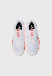 Baskets de sport blanches avec une tige en maille texturée, des accents rouges et une semelle à motif. Comprend des lacets, un logo sur la languette et un col rembourré.