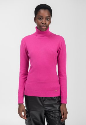 Pullover a collo alto in fucsia realizzato in morbido tessuto a maglia, con polsini e orlo a coste. Un piccolo logo metallico decorativo è posizionato in basso.