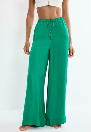 Zielone spodnie o szerokich nogawkach z wiązanym pasem, noszone przez osobę stojącą boso na tle jednolitego, jasnego tła.