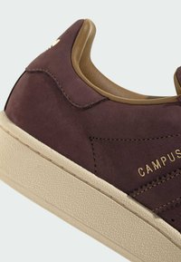 Brown suede sneaker with a beige textured sole, featuring a smooth brown interior and gold "CAMPUS" branding on the side.