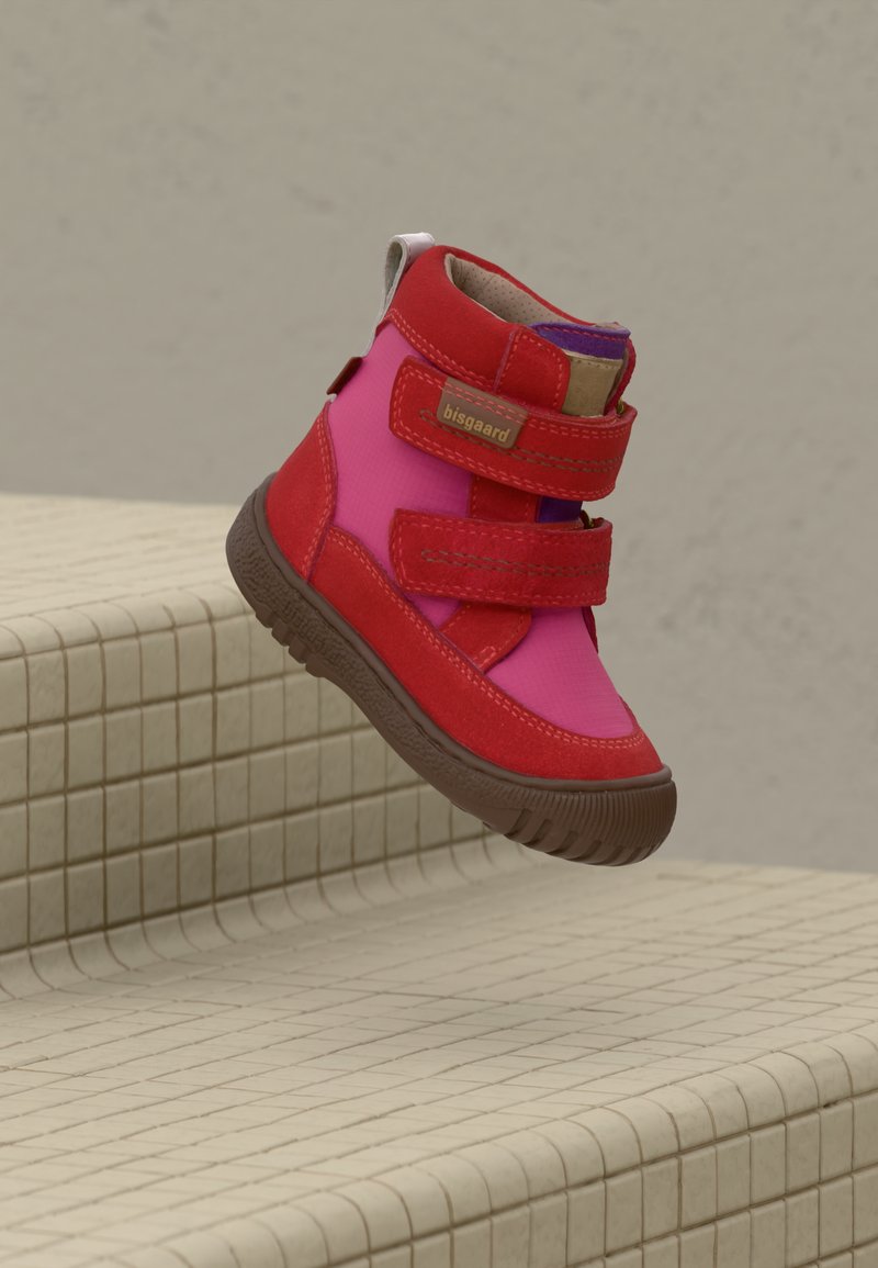 Røde og rosa barnesko med høy ankel, brun såle og doble borrelåser, svevende over beige flislagte trapper.