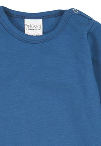 Blue cotton t-shirt with a round neckline, featuring a tag that reads "Fred's World." Includes a snap button at the shoulder for easy dressing.