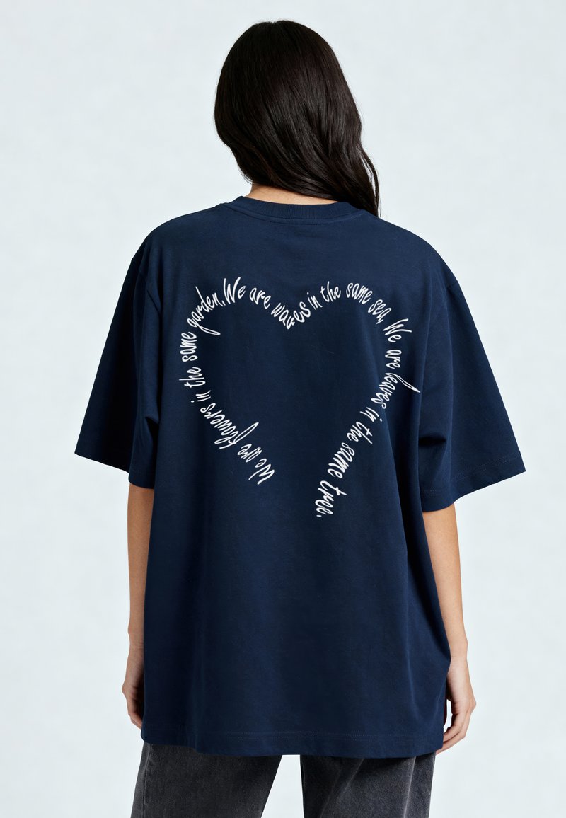 Tamsiai mėlynas per didelis medvilninis marškinėliai su balta tekstu širdies forma nugaroje, apvaliu iškirpimu ir trumpomis rankovėmis.