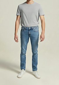 Jasnoszary t-shirt w połączeniu ze średnio niebieskimi jeansami denimowymi. Stopy w białych trampkach. Prosty design, luźny krój i minimalne detale.