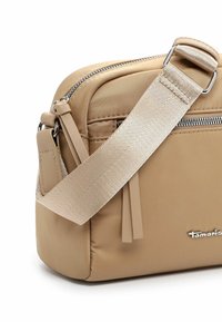 Borsa a tracolla in nylon beige con una texture liscia, caratterizzata da una zip argentata e una tracolla in tessuto regolabile. Etichetta con logo sulla parte anteriore.