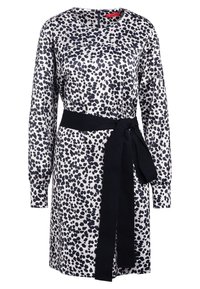 Robe blanche à manches longues avec des taches noires irrégulières, un col rond, une fermeture éclair au dos, et une large ceinture en tissu noir nouée à la taille.