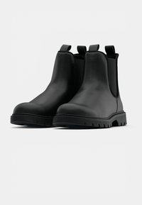 Botas Chelsea de cuero negro con paneles laterales elásticos, tiradores y suelas de goma resistentes. Textura suave con detalles de costura.