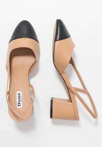 Beige leather slingback heels with a black pointed cap toe, featuring a block heel and an open design with crisscross straps.