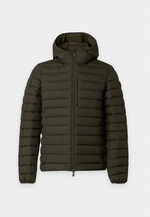 Homme portant une doudoune vert foncé avec capuche, un t-shirt blanc rayé, un jean bleu ample et des baskets marron, debout sur fond blanc.