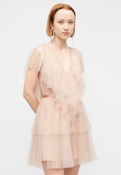 Φόρεμα από τούλι σε ροδακινί απόχρωση με στρωμένες βολάν, λαιμόκοψη V και εφαρμοστή μέση. Διαθέτει διάφανα καπαρτίνια μανίκια και απαλή υφή.