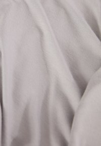 Tissu gris clair avec une texture lisse, présentant des lignes subtiles et des variations d'ombrage, se drapant doucement en plis.