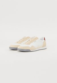Beige og hvite sko med semsket skinn og mesh-materialer, snøring, gummisåle og en liten brun detalj ved hælen.