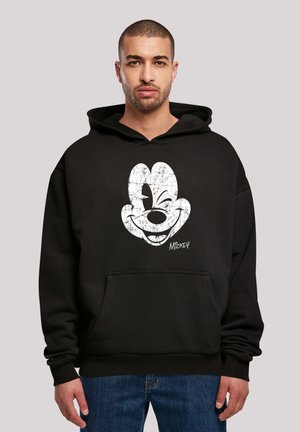 Svart hettegenser laget av myk stoff med et stort hvitt sprukket Mickey Mouse-motiv på forsiden, med kengurulomme og snorhette.