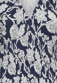 Tengerészkék szövet fehér, bonyolult virág- és levélmintákkal, begyűrt varrással egy V-nyak alatt.