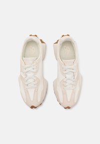Paire de baskets blanches et beiges avec des lacets blancs et des semelles en caoutchouc marron clair vues de dessus sur un fond blanc.
