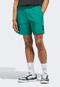 Turquoise korte broek van lichtgewicht stof met een zwart Adidas-logo patch. Gemaakt met witte sokken en navy sneakers, en toont een relaxte pasvorm.