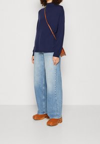 Mörkblå långärmad topp, ljusblå vida jeans och bruna träskor med metallspikar. Liten brun axelväska.