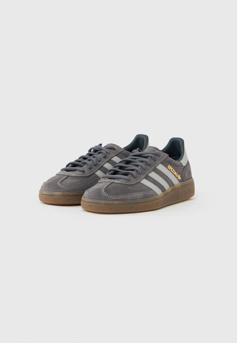 Gray suede sneakers with rubber outsole, featuring three white stripes and gold "Spezial" lettering on the side. Round toe, lace-up design.