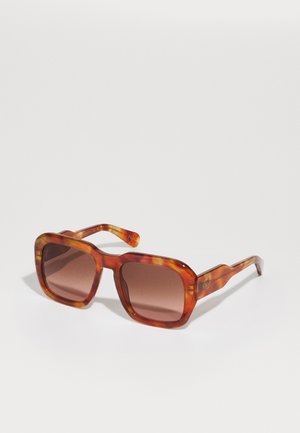 Gafas de sol de carey con un marco cuadrado, lentes tintados marrones y acentos de rayas marrones en las varillas. Marcadas con el logo en la patilla.