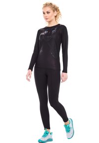 Svart långärmad atletisk topp med en grafik av en katts ansikte. I kombination med svarta tights och sneakers med turkosa detaljer.