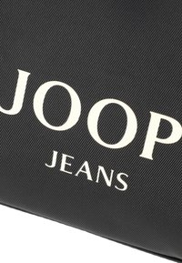 Czarna torba o fakturze z dużym białym napisem "JOOP JEANS". Materiał wydaje się trwały z paskowanym wzorem.