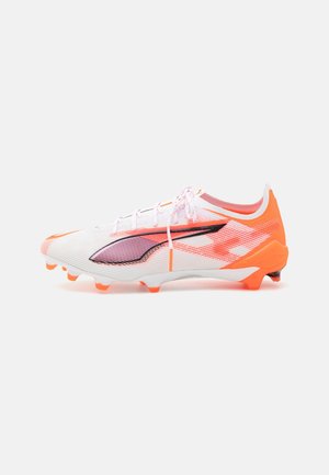 Botas de fútbol blancas con acentos naranjas, parte superior de malla y un detalle prominente en púrpura. Presenta un diseño aerodinámico y suela con clavos para mayor tracción.