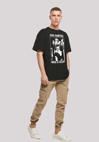 Black oversized t-shirt with a graphic print featuring cartoon villains. Beige cargo pants with pockets. White sneakers complete the outfit.