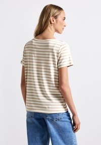 T-shirt beige clair à manches courtes avec des rayures, col rond, en tissu doux et coupe décontractée, associé à un jean en denim bleu.