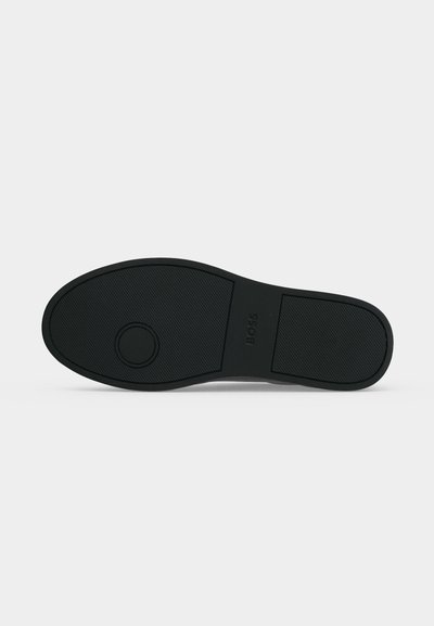 Semelle de chaussure en caoutchouc noir avec des motifs de grip texturés et un design circulaire près de l'avant, marqué "BOSS" au centre.