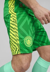 Zöld focinadrág sárga grafikus mintázattal az oldalán, Manchester City logóval, k önnyű, légáteresztő anyagból készült.