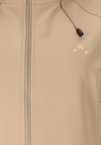 Beige Jacke mit Reißverschluss, kleinem dreieckigem Logo auf der Brust und verstellbarem Kordelzug mit schwarzem Knebel in der Nähe des Kragens.