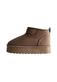 Bottines en suede marron avec un bout arrondi et une semelle épaisse et texturée. Comprend une couture sur le côté et une languette au talon.