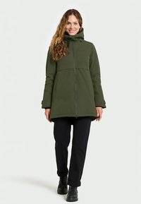 Green waterproof jacket with a hood, front zipper, and long sleeves, paired with black pants and boots; smooth fabric, mid-length design.
