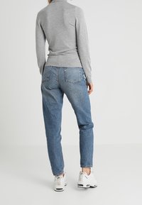 Maglione grigio a maniche lunghe abbinato a jeans blu a vestibilità ampia e scarpe da ginnastica bianche. Presenta polsini a costine e una texture lavorata a maglia.