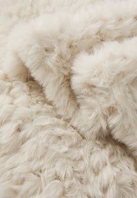Tissu en fausse fourrure douce et moelleuse de couleur blanc cassé avec une texture dense et de longues fibres duveteuses, présenté en gros plan.