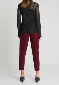 Top nero trasparente a maniche lunghe con costine verticali, abbinato a pantaloni tapered color borgogna. Sandali neri con tacco a blocco completano il look.