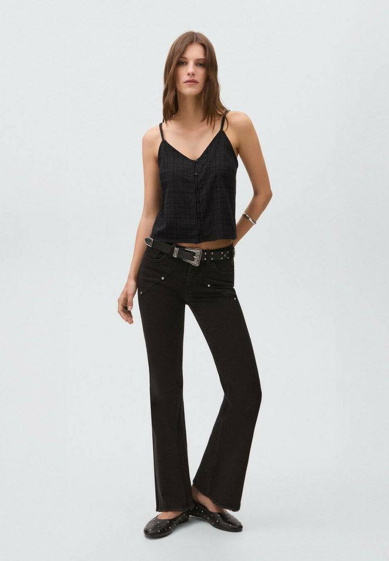 Svart kort croptop i en strukturerad tyg, kombinerad med högmidjade svarta utsvängda jeans med dekorativa nitar och ett silverbälte.