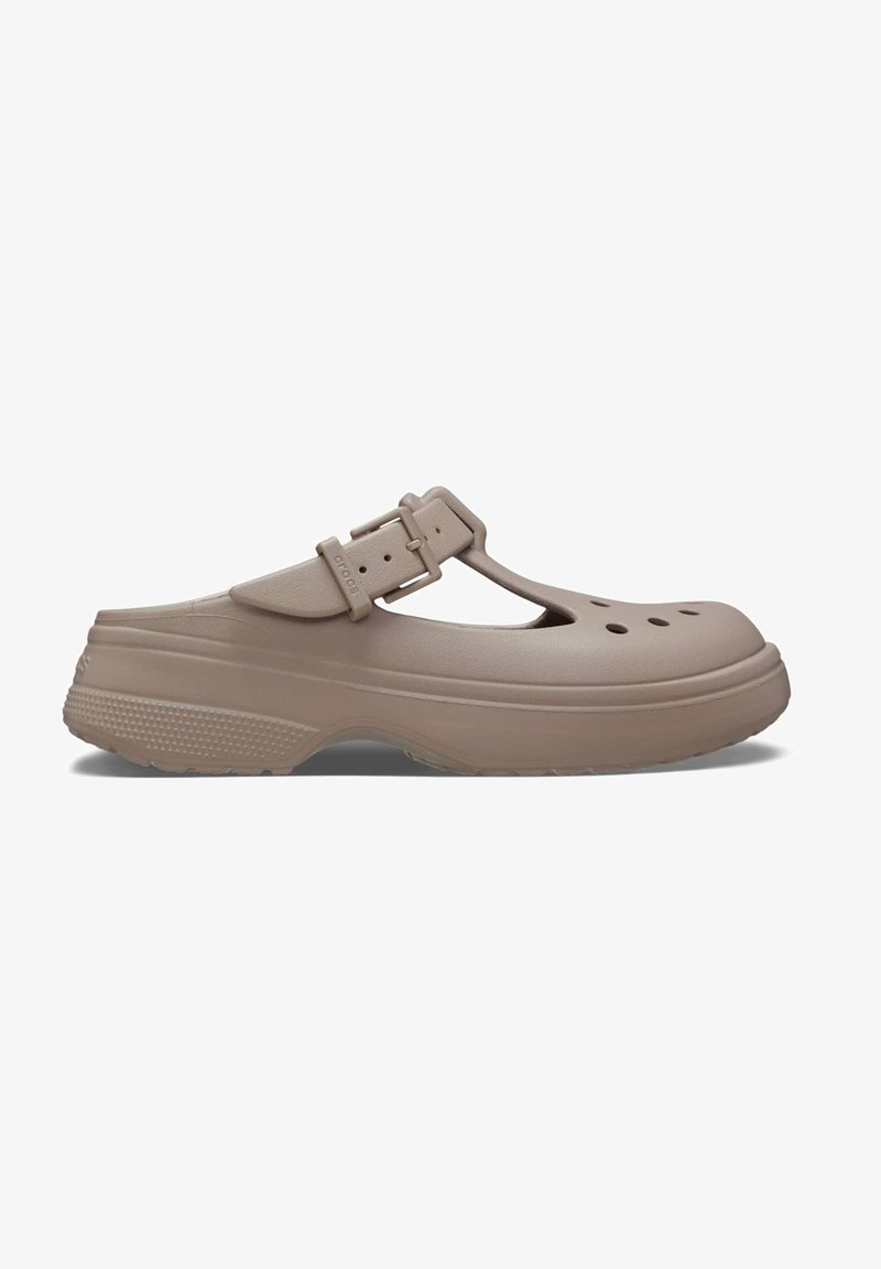 Sabots en caoutchouc beige avec un design à sangle T et une boucle réglable, comportant des trous de ventilation et une semelle texturée pour une meilleure adhérence.