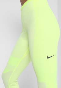 Leggings amarillos neón con un ajuste ceñido, que presentan paneles de malla, una cinturilla elástica y un pequeño logo negro de Nike en un lado.