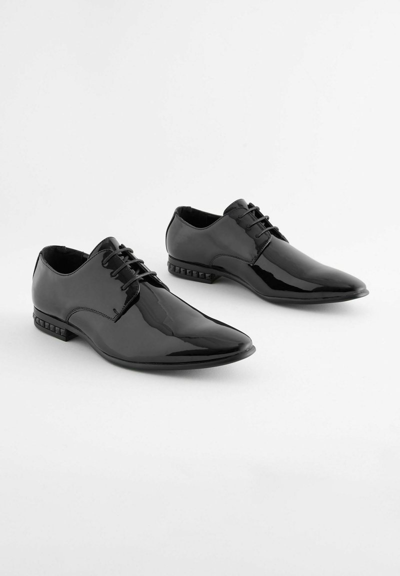 Schwarze Lackleder-Oxfords mit spitzem Zehenbereich, Schnürung und strukturierten Absatzakzenten. Glatte Oberfläche und elegantes Design.